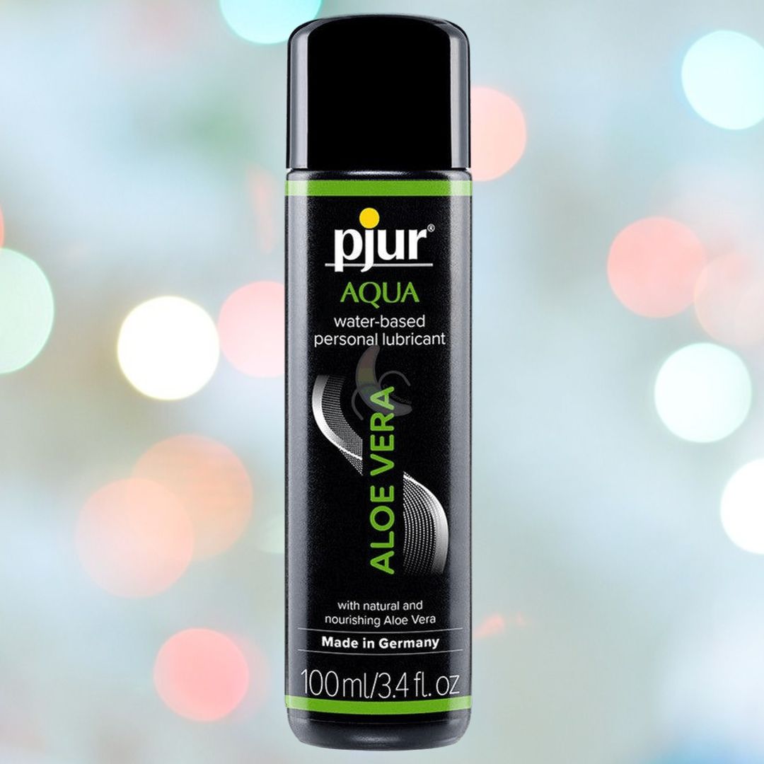 A bottle of Pjur Aqua Water-Based Lube with Aloe Vera (3.4oz) is pictured against a blurred background dotted with circular light spots. The label states that it is a water-based personal lubricant made in Germany and enriched with natural, nourishing Aloe Vera—ideal for enhancing your favorite sex toy experience.