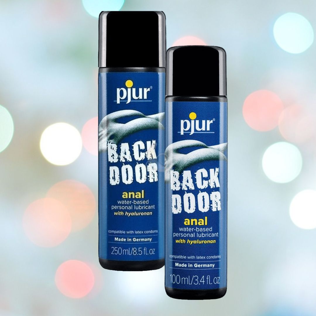 Two bottles of Pjur Backdoor Comfort Water-Based Anal Glide, one 250ml and the other 100ml in blue, are showcased against a bokeh background of soft, colorful lights. These products from Pjur are enriched with hyaluronan for enhanced moisturization.