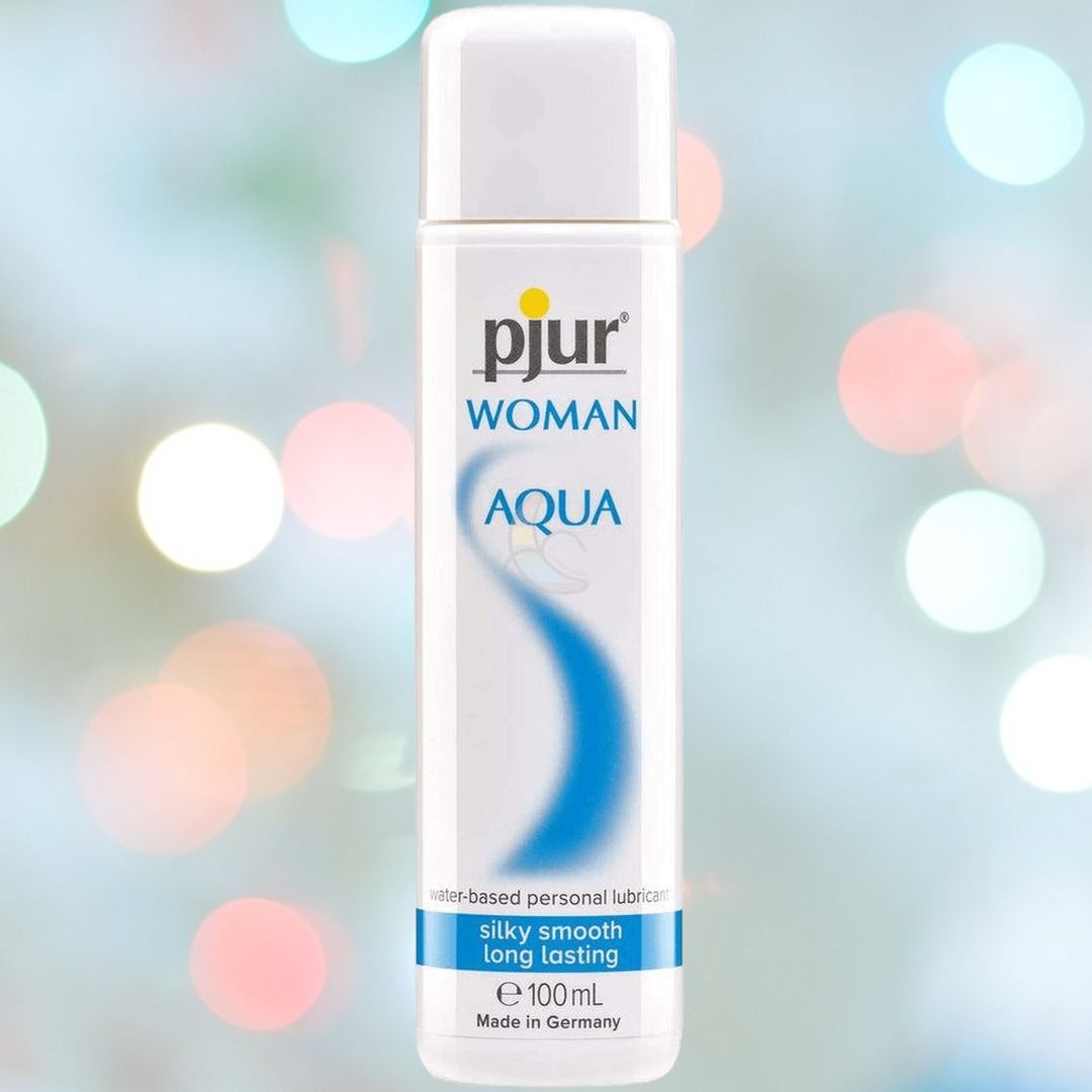 The image features a white bottle labeled "Pjur Woman Aqua Personal Lubricant | 3.4oz" from the brand Pjur, set against a blurred, colorful background. This water-based lubricant is described as silky smooth and long-lasting, offering moisturizing properties and crafted in Germany.