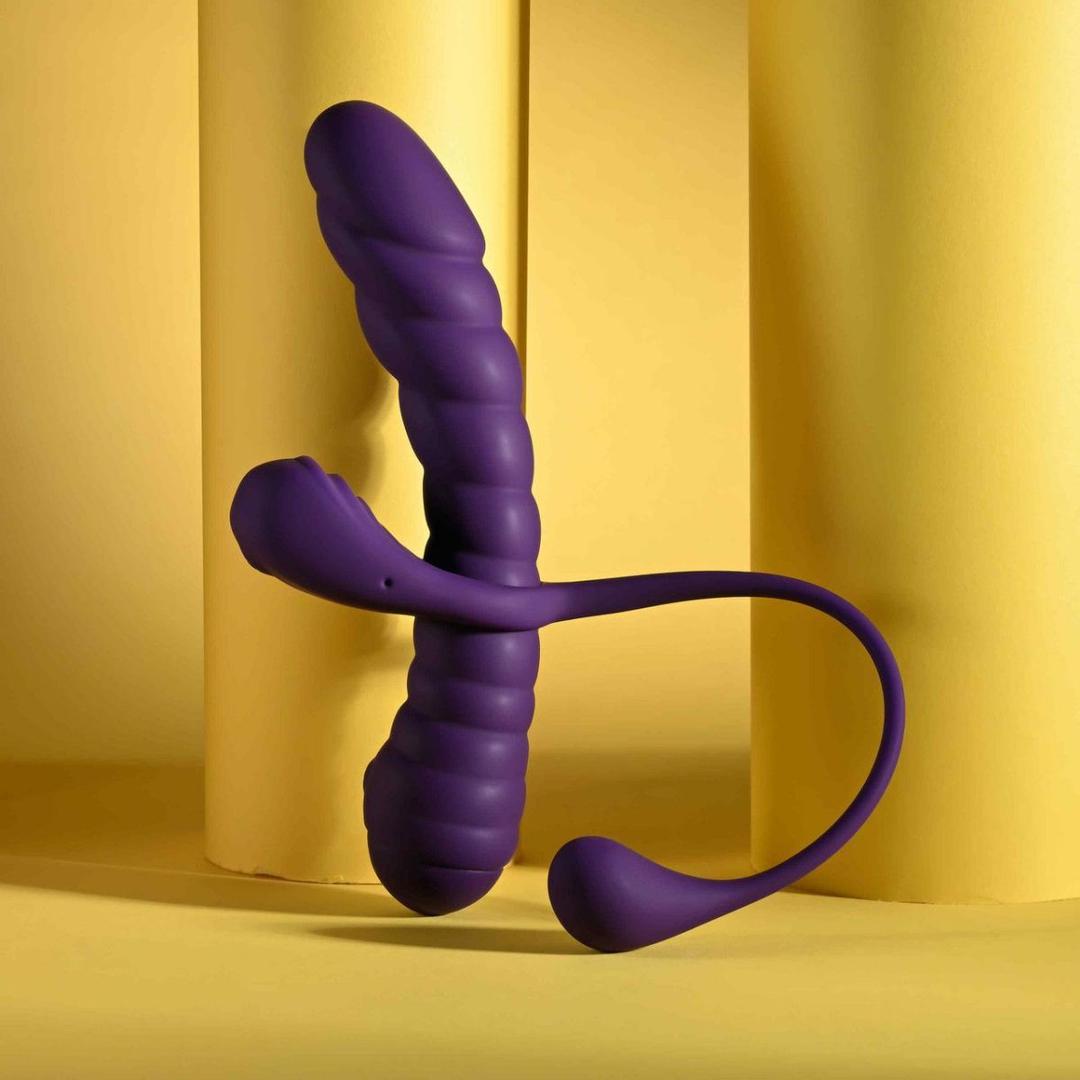 The Playboy Twisted Playground by Evolved Novelties, a purple silicone dual-ended toy with a ribbed, textured design, stands upright against a yellow background with cylindrical columns.