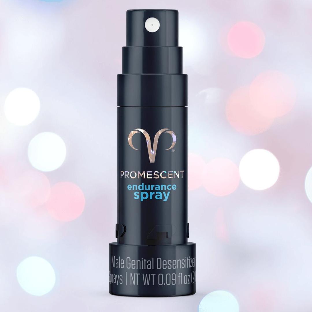 A black bottle of Promescent Desensitizing Endurance Spray for Men by Promescent, labeled “Male Genital Desensitizer” and featuring Anti-Transfer technology, stands out against a backdrop of blurred pink and white lights.