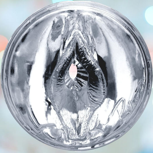 A close-up photo of the clear, cylindrical Fleshlight Quickshot Riley Reid Open-Ended Masturbation Sleeve, showcasing its intricate, textured design resembling a deep, geometric pattern. The background features blurred soft pastel-colored lights creating a beautiful bokeh effect. 1080