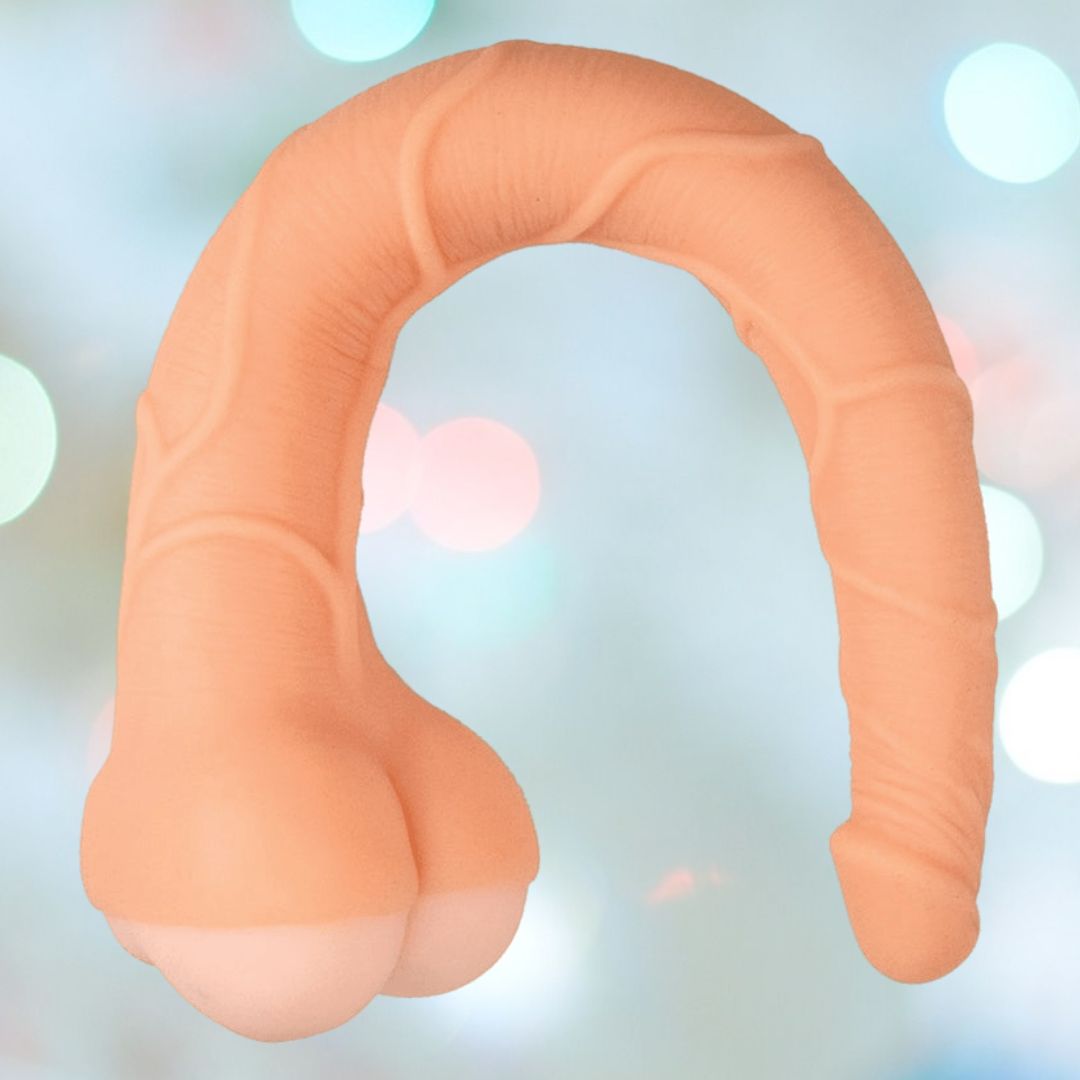 Displayed against a blurred background of blue, white, and pink lights is the RealCocks Penis Masturbator 14" 3-in-1 - Light by Nasstoys. This item features a segmented, curved shape crafted from ultra-soft TPE material in a beige hue.