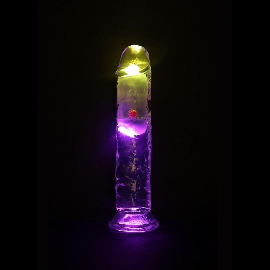 The RealRock Wireless Rechargeable LED Vibrating 7" by Shots America, a transparent dildo with yellow and purple LED lights inside, stands upright against a black background.
