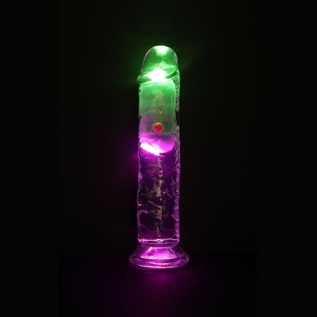 The RealRock Wireless Rechargeable LED Vibrating 7" by Shots America stands upright, glowing with green and purple LEDs against a dark background.