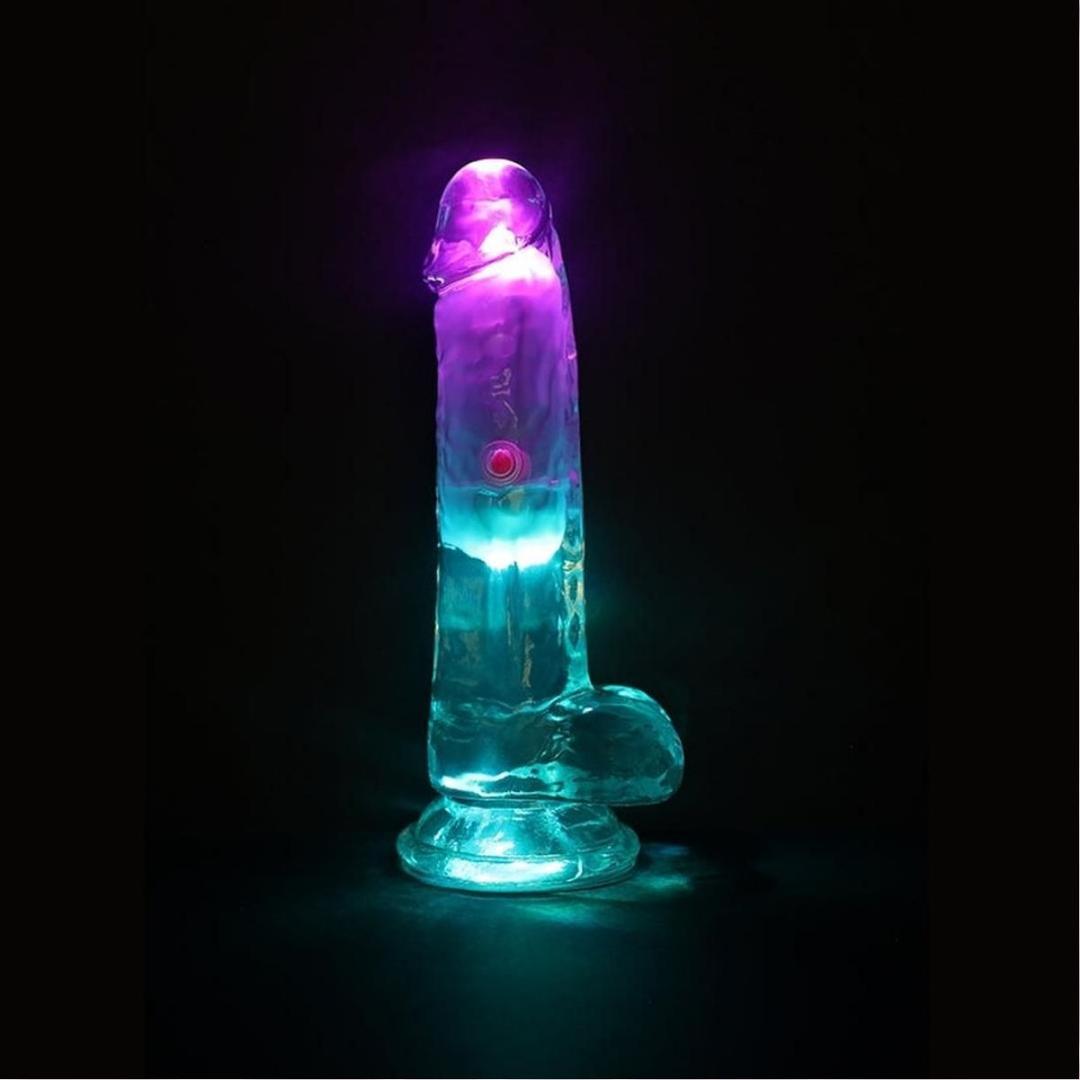 The RealRock Wireless Rechargeable LED Vibrating With Balls 6" by Shots America is illuminated in purple and blue against a dark backdrop, showcasing its sleek, realistic form.