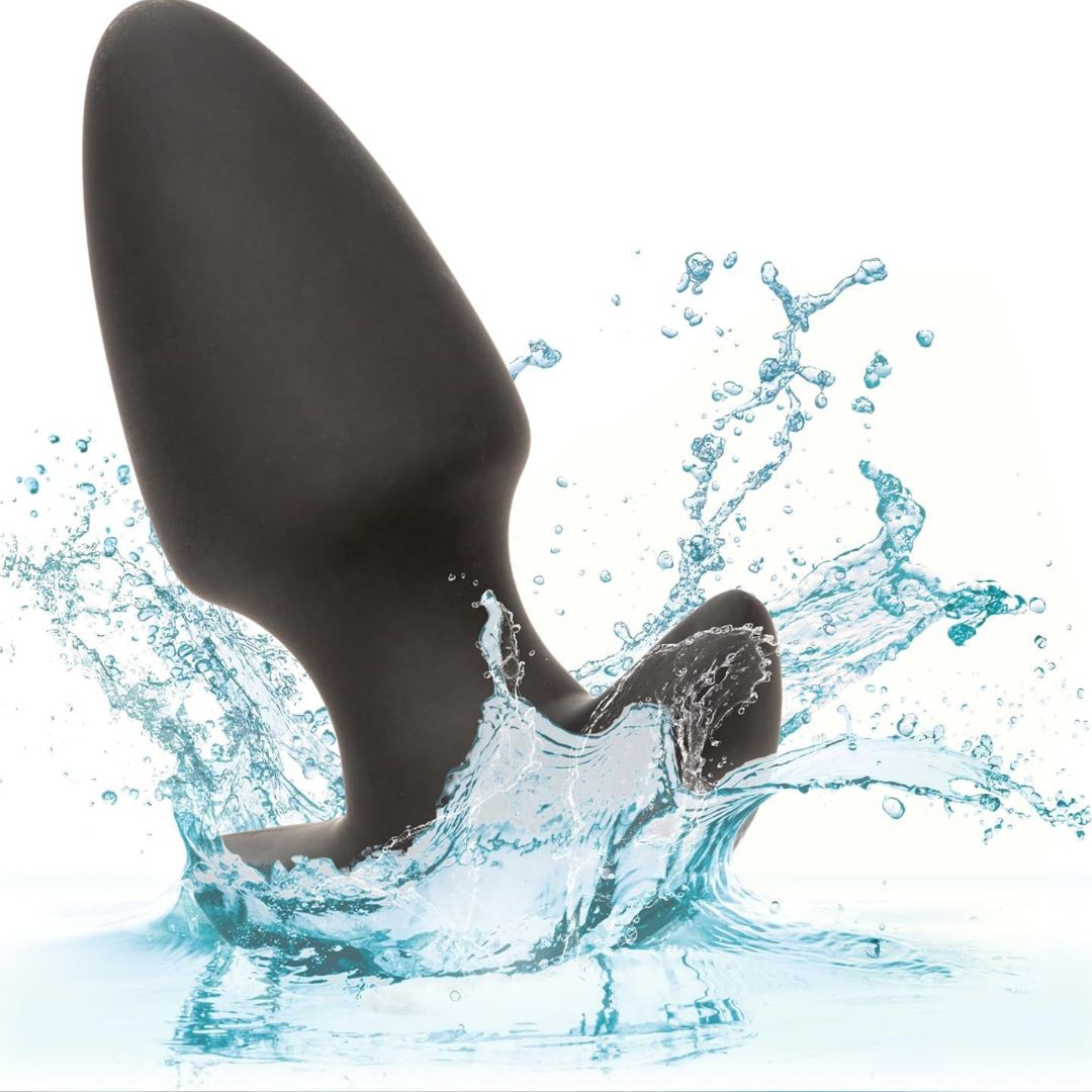 The CalExotics Rock Bottom Thrusting Probe—a black silicone plug—partially submerged in water with splashes surrounding it, shown against a white background.