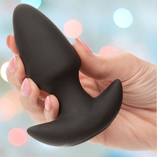 A hand with pink manicured nails holds the black CalExotics Rock Bottom Thrusting Probe against a softly blurred, colorful background. 1080