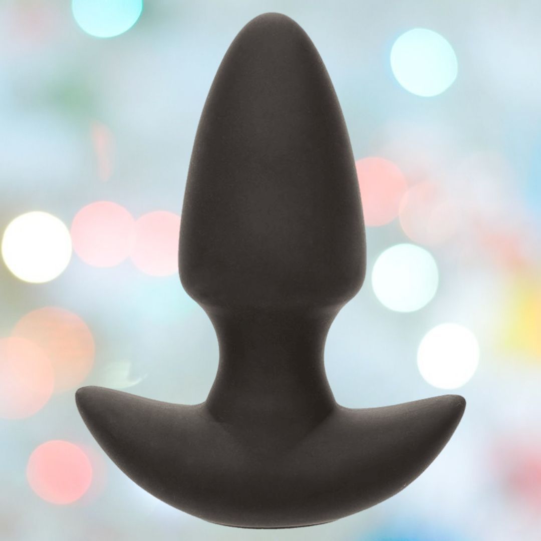 The CalExotics Rock Bottom Thrusting Probe, a black silicone butt plug with a tapered tip and flared base, stands upright against a blurred backdrop with pastel bokeh lights.