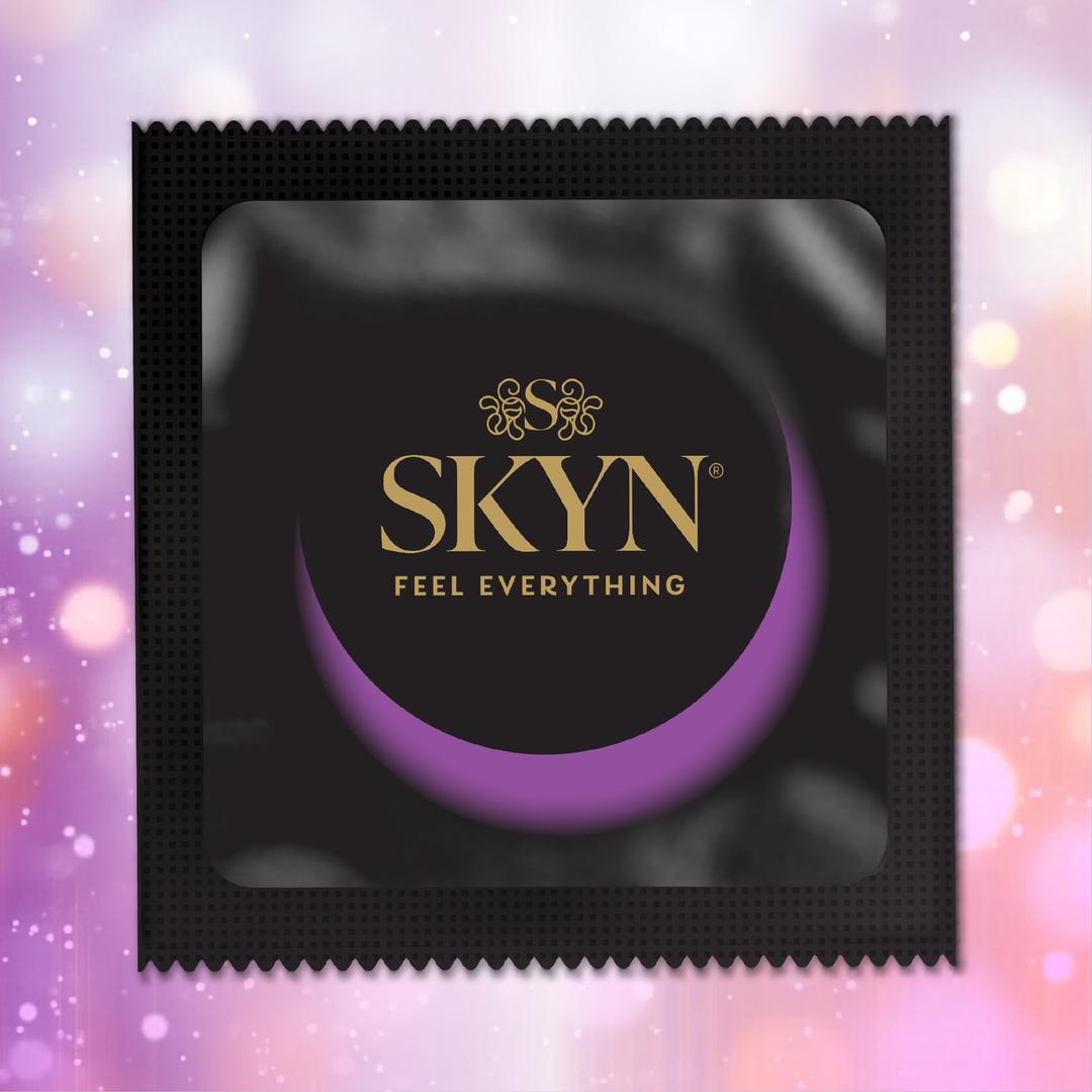 A black LifeStyles SKYN Elite Condoms (Latex-Free) wrapper, featuring gold "SKYN Feel Everything" text and a purple crescent, stands out against a soft pink and violet blurred background—emphasizing these ultra-thin condoms for heightened sensation.