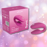 A We-Vibe Sync 2 Couples Vibrator with App in Rose by We-Vibe is displayed alongside its matching product box, set against a soft, purple and pink bokeh background.