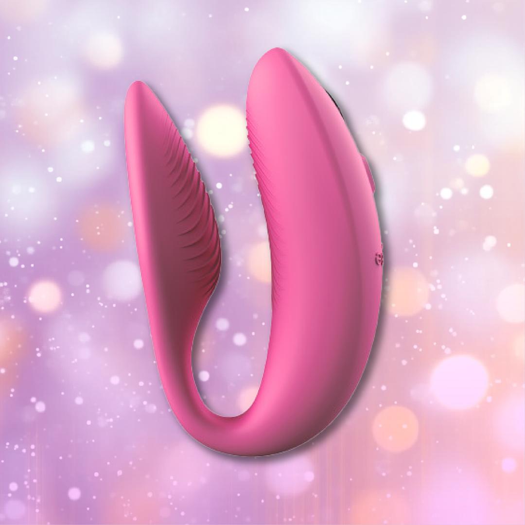 The We-Vibe Sync 2 Couples Vibrator with App in Rose, a U-shaped vibrator by We-Vibe featuring textured inner surfaces, is shown against a pastel bokeh background.
