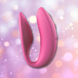 The We-Vibe Sync 2 Couples Vibrator with App in Rose, a U-shaped vibrator by We-Vibe featuring textured inner surfaces, is shown against a pastel bokeh background.