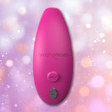A rose-colored, oval-shaped We-Vibe Sync 2 Couples Vibrator with App, featuring a button and metallic accent, is displayed against a pastel bokeh background. This We-Vibe product blends elegant design with cutting-edge remote control features for intimate connection.