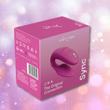 A We-Vibe Sync 2 Couples Vibrator with App - Rose product box featuring an image of the couples vibrator on the front, displayed against a softly blurred purple and pink background with gentle light bokeh effects.