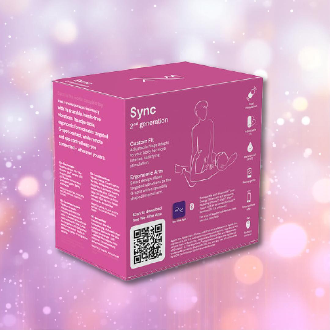 A rose-colored box labeled "We-Vibe Sync 2 Couples Vibrator with App" features playful illustrations, icons, and instructions for the wearable couples vibrator. Displayed against a soft pink background with gentle white bokeh light effects, the packaging highlights the innovative We-Vibe Sync 2 by We-Vibe—a remote control vibrator designed to enhance intimacy and wellness.