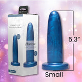 The Fleshlight HerSpot Cobalt Lily Dildo, a 5.3-inch blue toy by Fleshlight, stands beside its packaging featuring product imagery and branding, set against a pink and purple blurred background.
