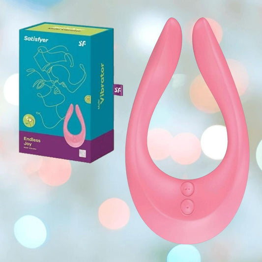 The Satisfyer Endless Joy Vibrator for Couples - Pink by Satisfyer is shown next to its teal and pink packaging, set against a soft, bokeh light background. 1080