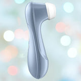 The Satisfyer Pro 2 Air Pulse Clitoral Stimulator by Satisfyer is shown in blue with a white brush head, set against a softly blurred pastel background featuring circular light spots.