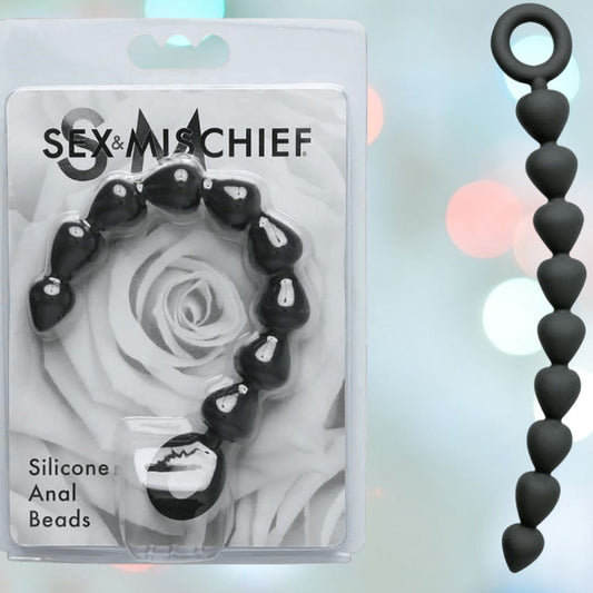 A package of Sportsheets' "Sex & Mischief Silicone Anal Beads" displays heart-shaped, black silicone beads ideal for backdoor exploration with a hint of elegance. The background features softly blurred colored lights. 1080