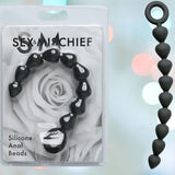 A package of Sportsheets' "Sex & Mischief Silicone Anal Beads" displays heart-shaped, black silicone beads ideal for backdoor exploration with a hint of elegance. The background features softly blurred colored lights.