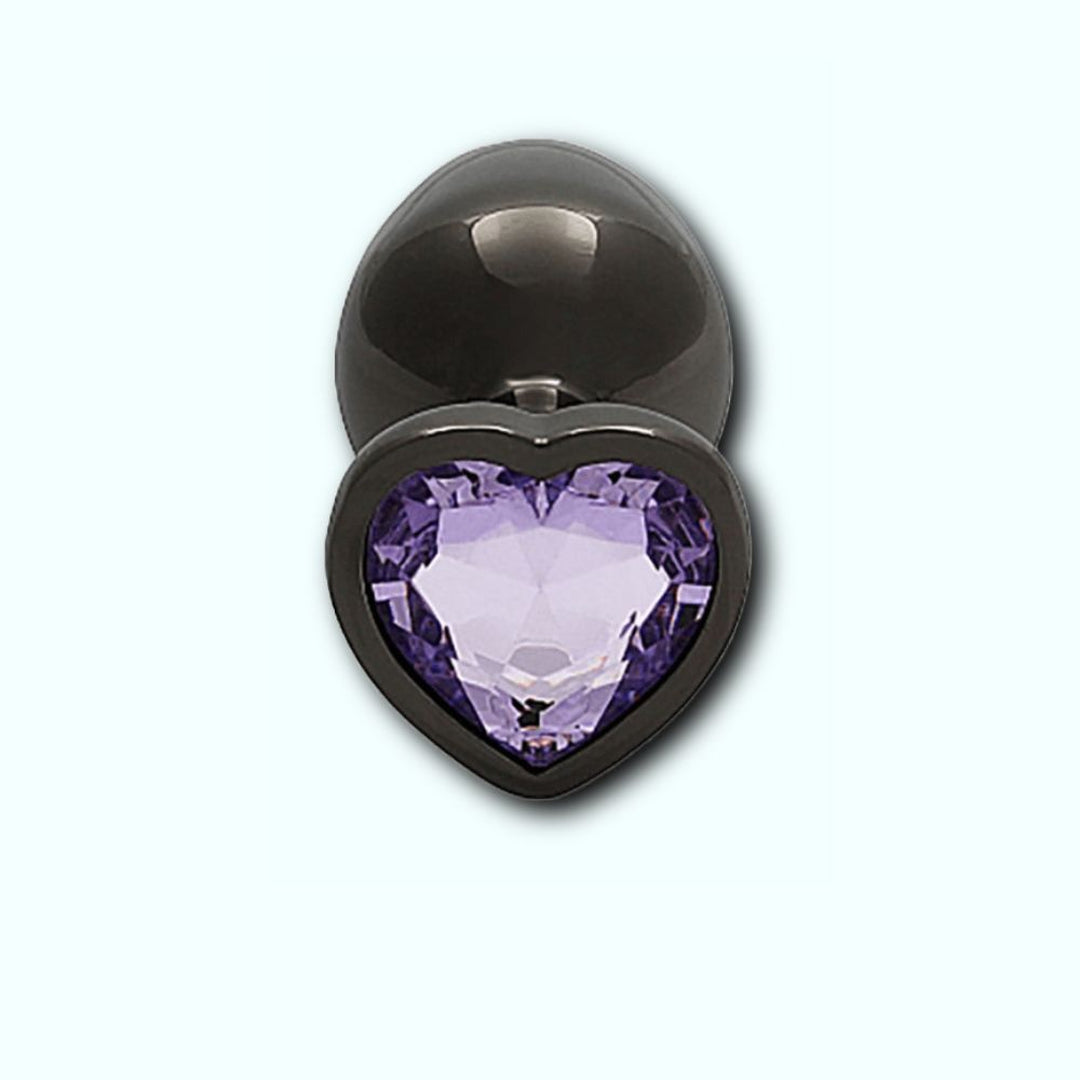 The Shots Ouch! Heart Gem Butt Plug Medium in Gunmetal/Amethyst is a medium-sized dark gray metal plug designed with a heart-shaped, jewel-encrusted base featuring a captivating, faceted amethyst gem at its center. The precision-cut gem reflects light to create a dazzling sparkle, all set against the backdrop of a light, solid color.