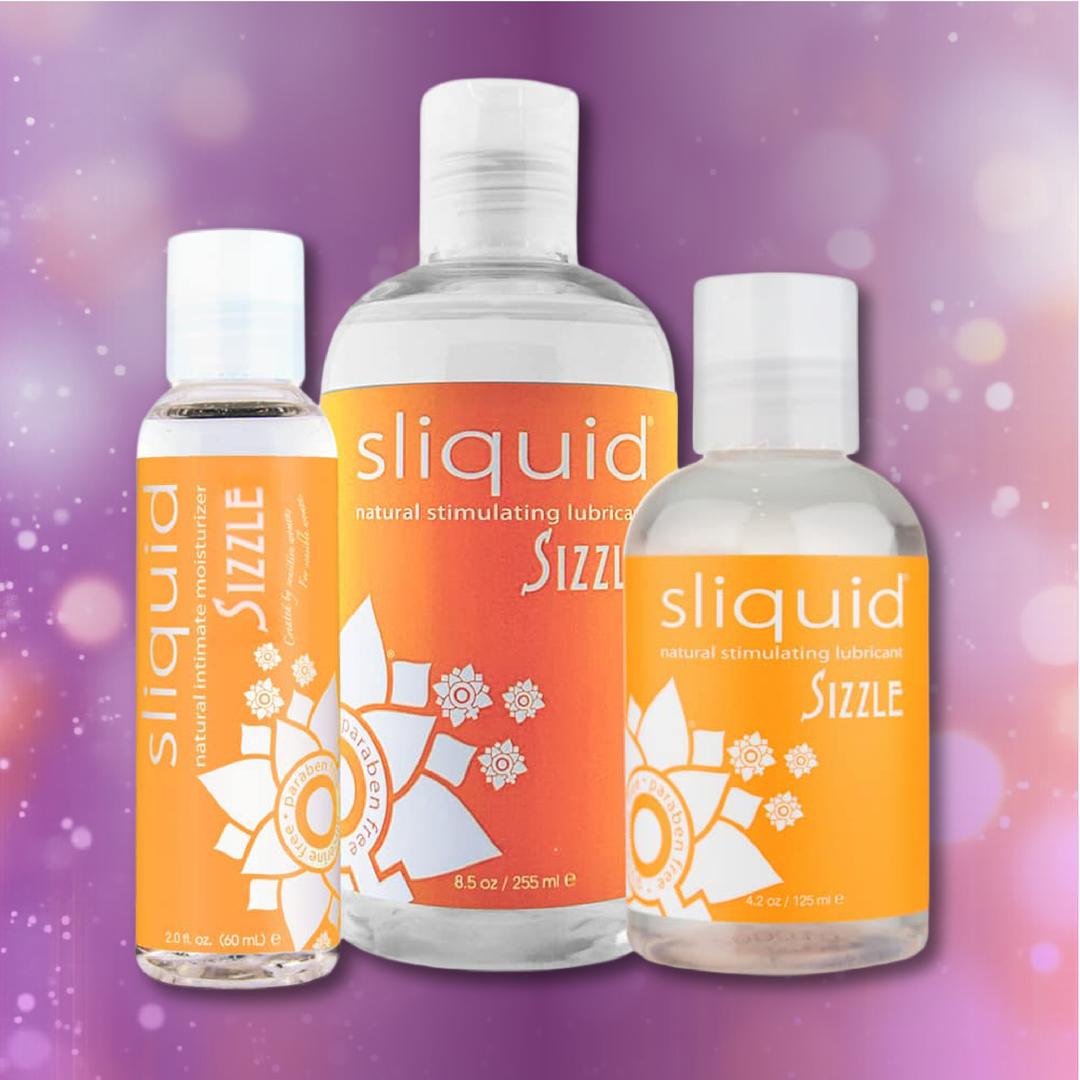 Three bottles of Sliquid Naturals ‘Sizzle’ Warming Lubricant by Sliquid, each featuring orange labels, are displayed on a pink and purple blurred background.