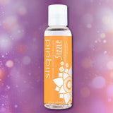 A 2 oz bottle of Sliquid Naturals ‘Sizzle’ Warming Lubricant by Sliquid, featuring an orange label, is set against a softly blurred purple background with bokeh light effects, highlighting the inviting appeal of this water-based warming lubricant.