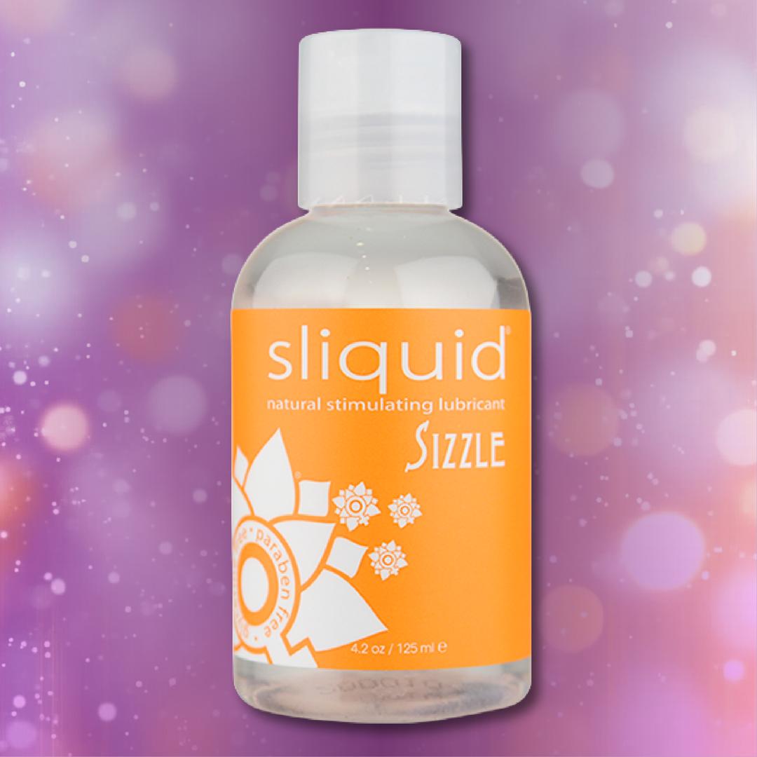 A clear bottle of Sliquid Naturals ‘Sizzle’ Warming Lubricant by Sliquid, featuring an orange label, set against a pink and purple bokeh background.