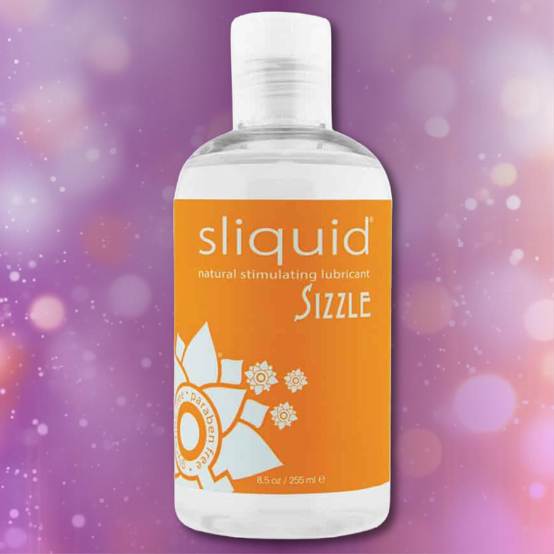 A bottle of Sliquid Naturals ‘Sizzle’ Warming Lubricant from Sliquid, featuring an orange label, rests against a purple bokeh background.