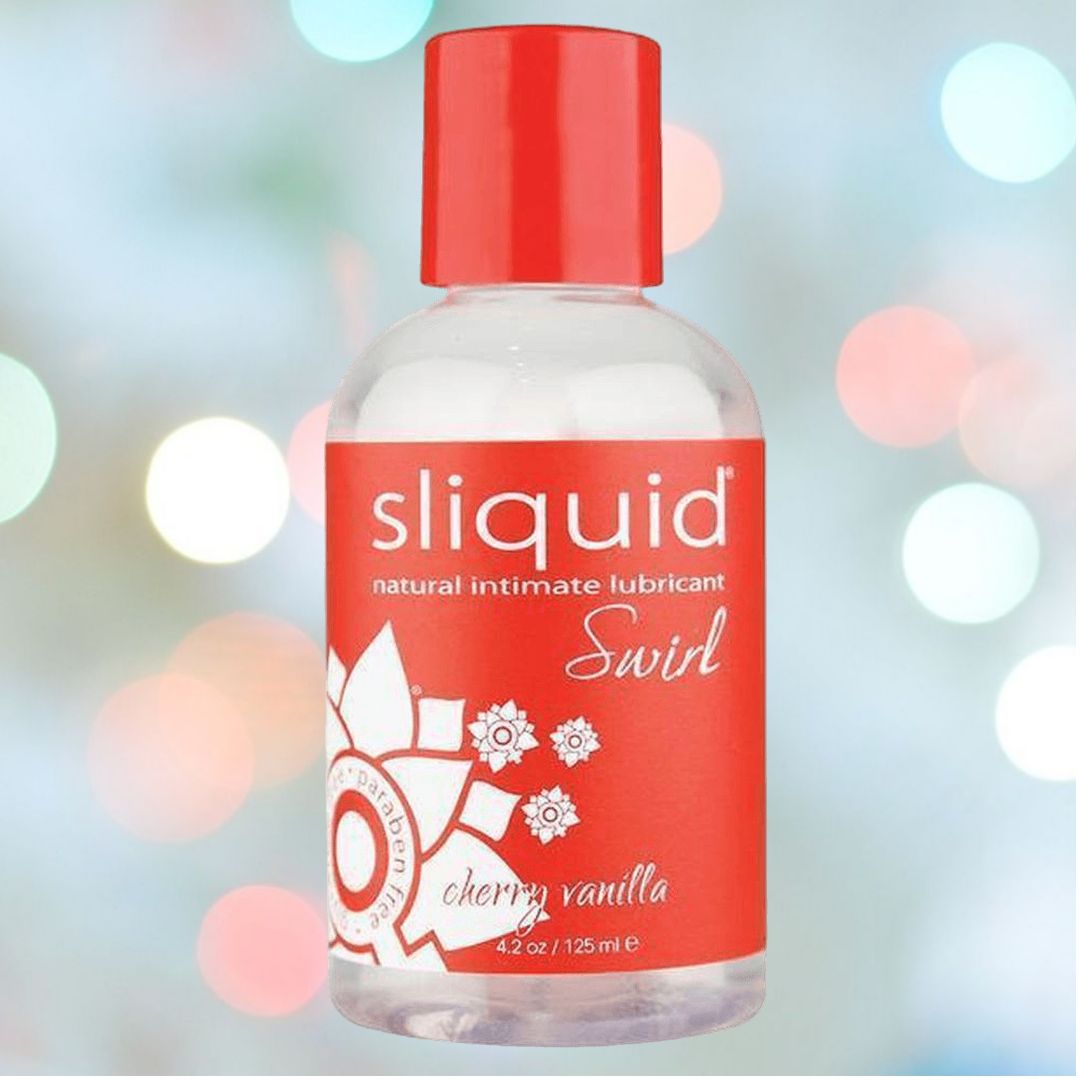 The Sliquid Naturals Cherry Vanilla Flavored Lubricant 🍒 | 4.2oz, with its distinctive red label and cap, is artfully displayed against a gentle bokeh backdrop of white and pastel circles. This charming water-based lubricant from Sliquid is ideal for enhancing intimate moments.