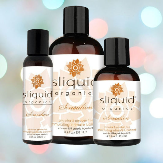 Three bottles of Sliquid's Organics Sensation Aloe-Based Warming Lube are displayed against a softly blurred background with multicolored lights. The labels emphasize its formula, which is free from glycerin and parabens, and made with 95% organic ingredients. 1080