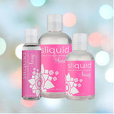 Three bottles of Sliquid Sassy Ultra-Thick Lubricant, ideal for use as an anal gel, in different sizes are showcased against a gentle, colorful bokeh backdrop. The bottles have pink labels decorated with floral motifs.