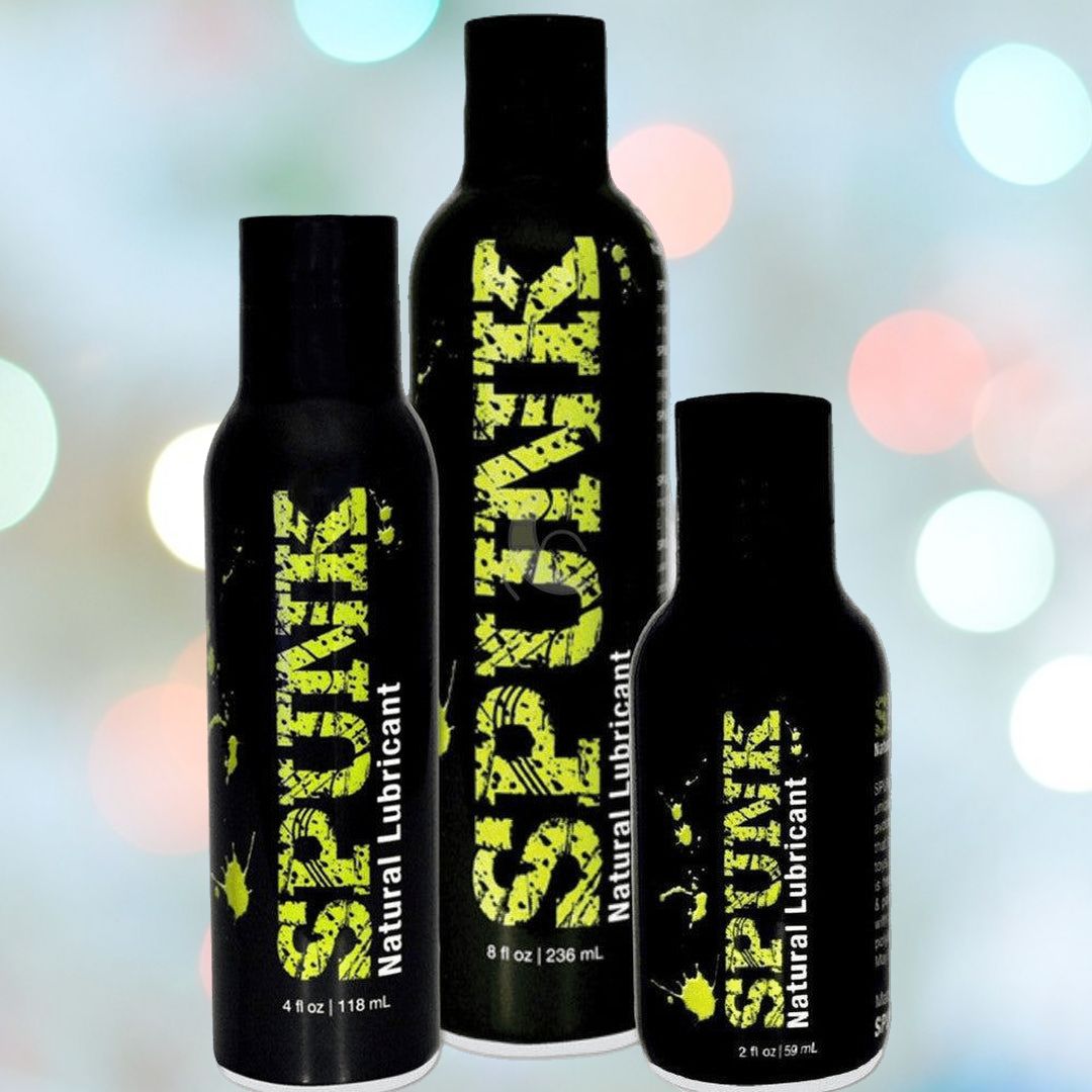 Three black bottles of various sizes with green text on them, labeled "SPUNK Natural Coconut and Avocado Oil Lubricant." The background is softly blurred with multicolored bokeh lights. Available in 2 fl oz, 4 fl oz, and 8 fl oz sizes, this vegan-friendly lubricant from Spunk Lube ensures a smooth experience every time.