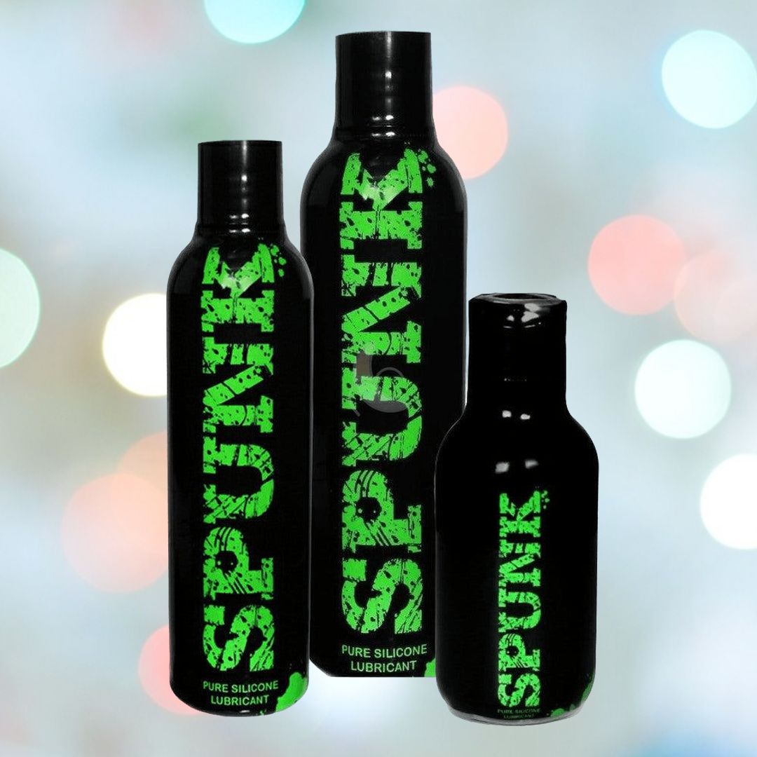 Three bottles of SPUNK Pure Silicone Lubricant, set against a blurred background with soft, colorful lights. The black bottles prominently display the brand name "Spunk Lube" in large green letters. Renowned for its hypoallergenic, long-lasting slippery texture, the lineup features varying sizes with the tallest on the left.