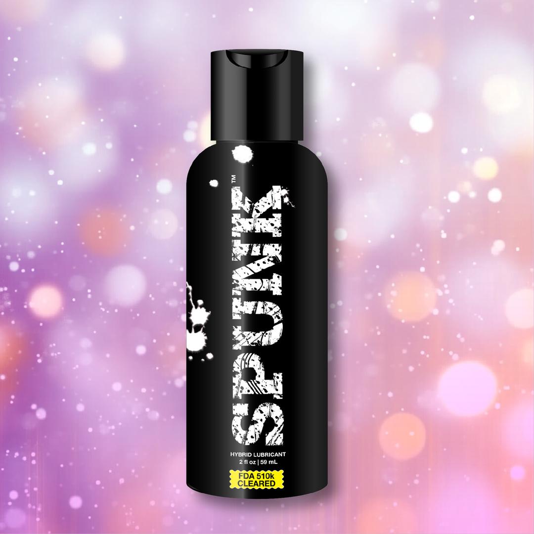 A black bottle labeled "SPUNK Hybrid Lubricant" from Spunk Lube, featuring a white splatter design, is centered against a blurred pastel background with soft bokeh effects.