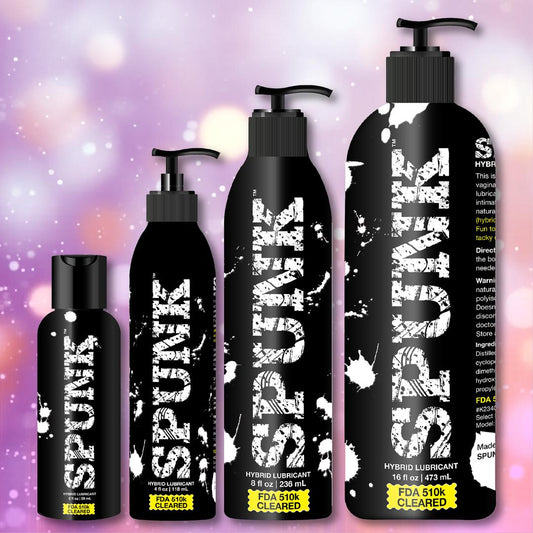 Four black bottles of Spunk Lube's SPUNK Hybrid Lubricant are lined up against a soft, colorful bokeh background. The largest has a pump dispenser. Each label reads “FDA 510K CLEARED.”. 1080