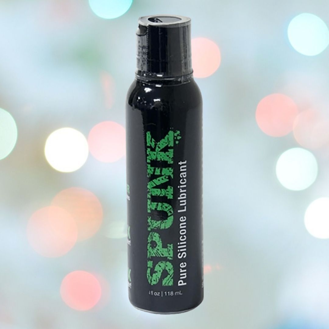 A black bottle of SPUNK Pure Silicone Lubricant, a product by Spunk Lube, is showcased against a blurred, multicolored light background. The 118 mL (4 fl oz) bottle with bold green text is renowned for its long-lasting slippery texture and hypoallergenic properties.