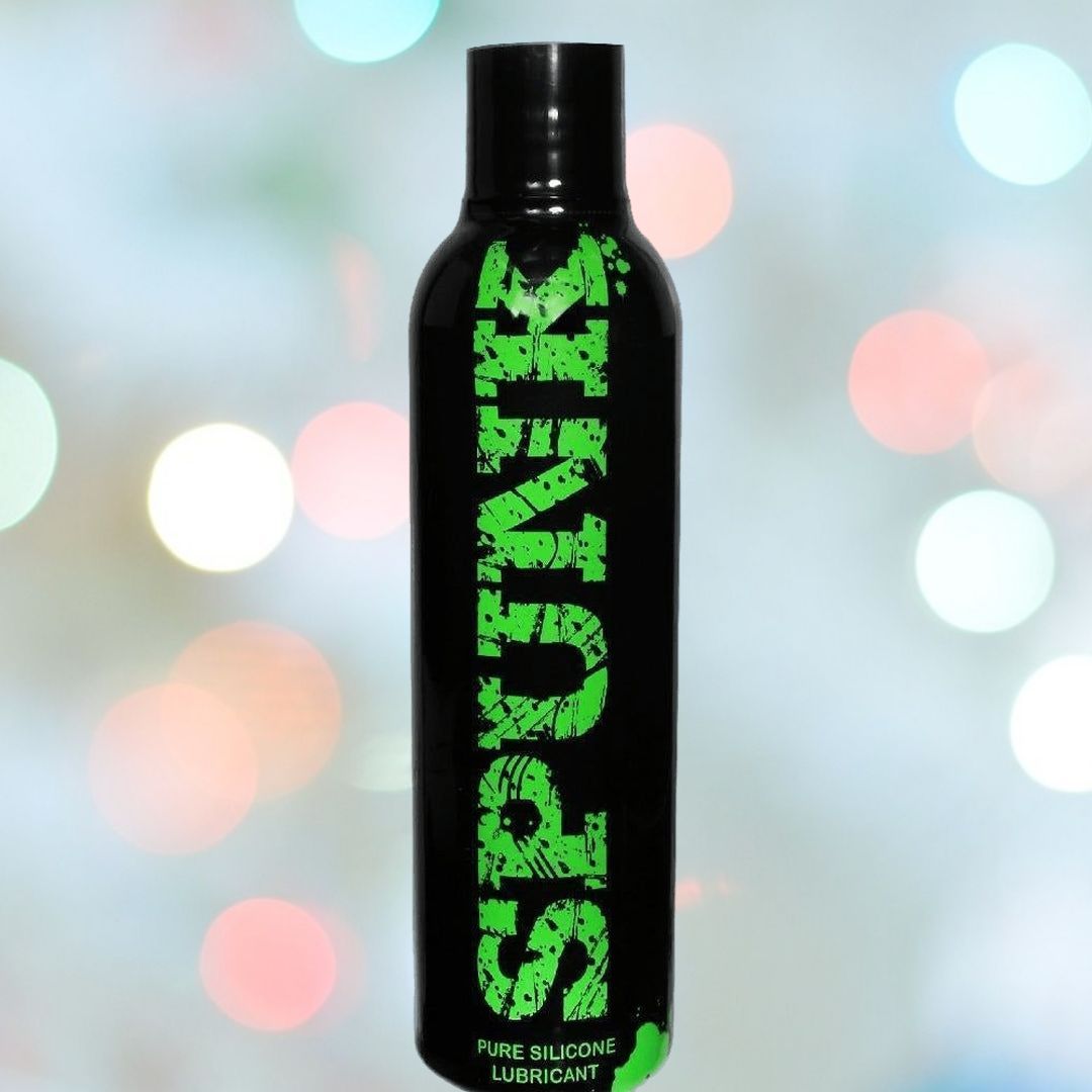 A black bottle of Spunk Lube's SPUNK Pure Silicone Lubricant with green text stands against a blurred background of multicolored bokeh lights, showcasing its hypoallergenic formula and long-lasting slippery texture.