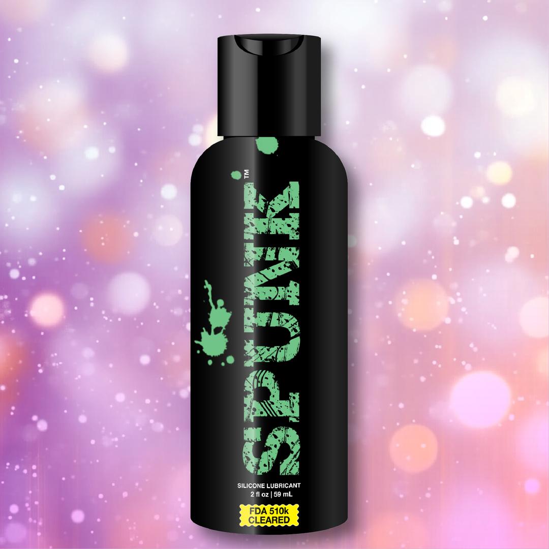 A black bottle labeled "SPUNK" stands against a pink and purple bokeh background. SPUNK Pure Silicone Lubricant by Spunk Lube is a long-lasting, FDA 510k cleared personal lube with a 2 fl oz (59 mL) capacity.