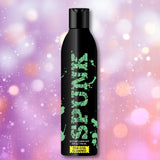 A black bottle labeled "SPUNK Pure Silicone Lubricant" by Spunk Lube, featuring a green splatter design, stands upright against a pink and purple bokeh background, emphasizing its long-lasting effects.