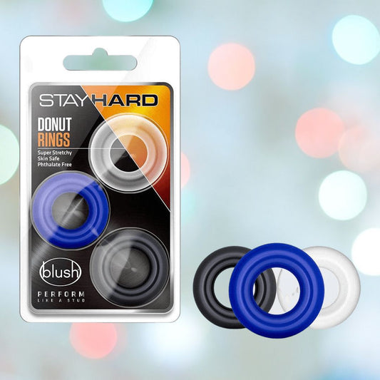 The "Stay Hard Donut Cock Rings (3-Pack)" by Blush Novelties come in black, blue, and transparent colors. The packaging features a soft-focus backdrop of colored lights, creating the perfect mood for addressing challenges such as premature ejaculation with flair and assurance. 1080