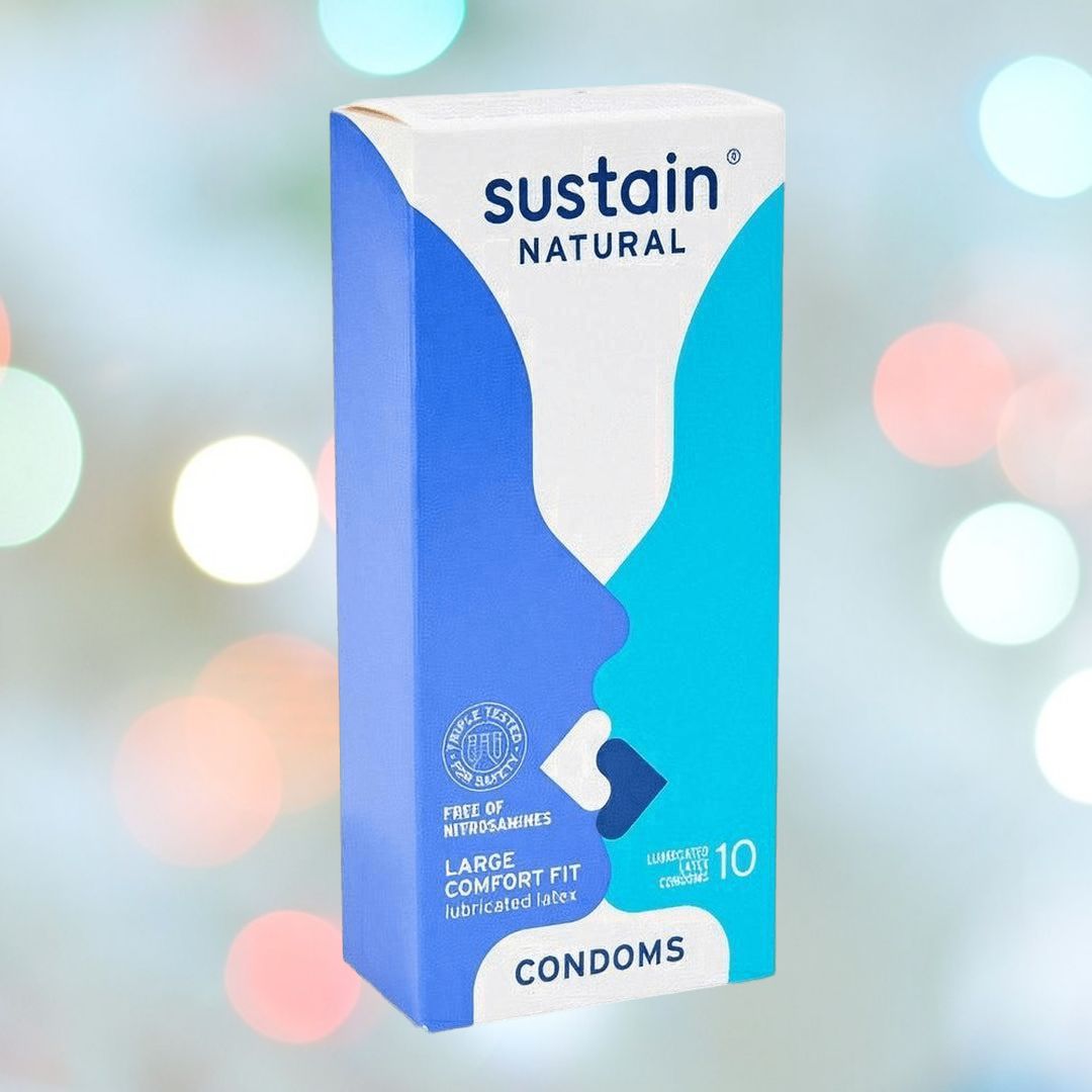 Box of Sustain Condoms' Comfort Fit Large Size Vegan Condoms, made from natural latex with a stylish blue and white design. Key features include "Large Comfort Fit," "Vegan Condoms," and "Free of Nitrosamines." Each box contains 10 lubricated condoms. The background is adorned with playful, blurry multicolored lights.