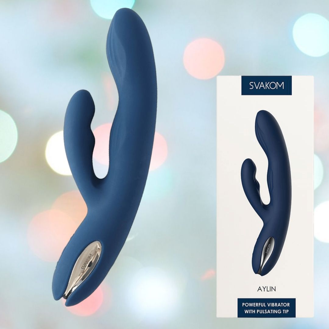 A dark blue dual-stimulation personal massager with a silver base is showcased next to its packaging. The box prominently displays the brand name "Svakom" and the product name "Svakom Aylin Rabbit Vibrator - Dark Blue," featuring a powerful rabbit vibrator with a pulsating G-spot tip and various vibration modes for enhanced pleasure.