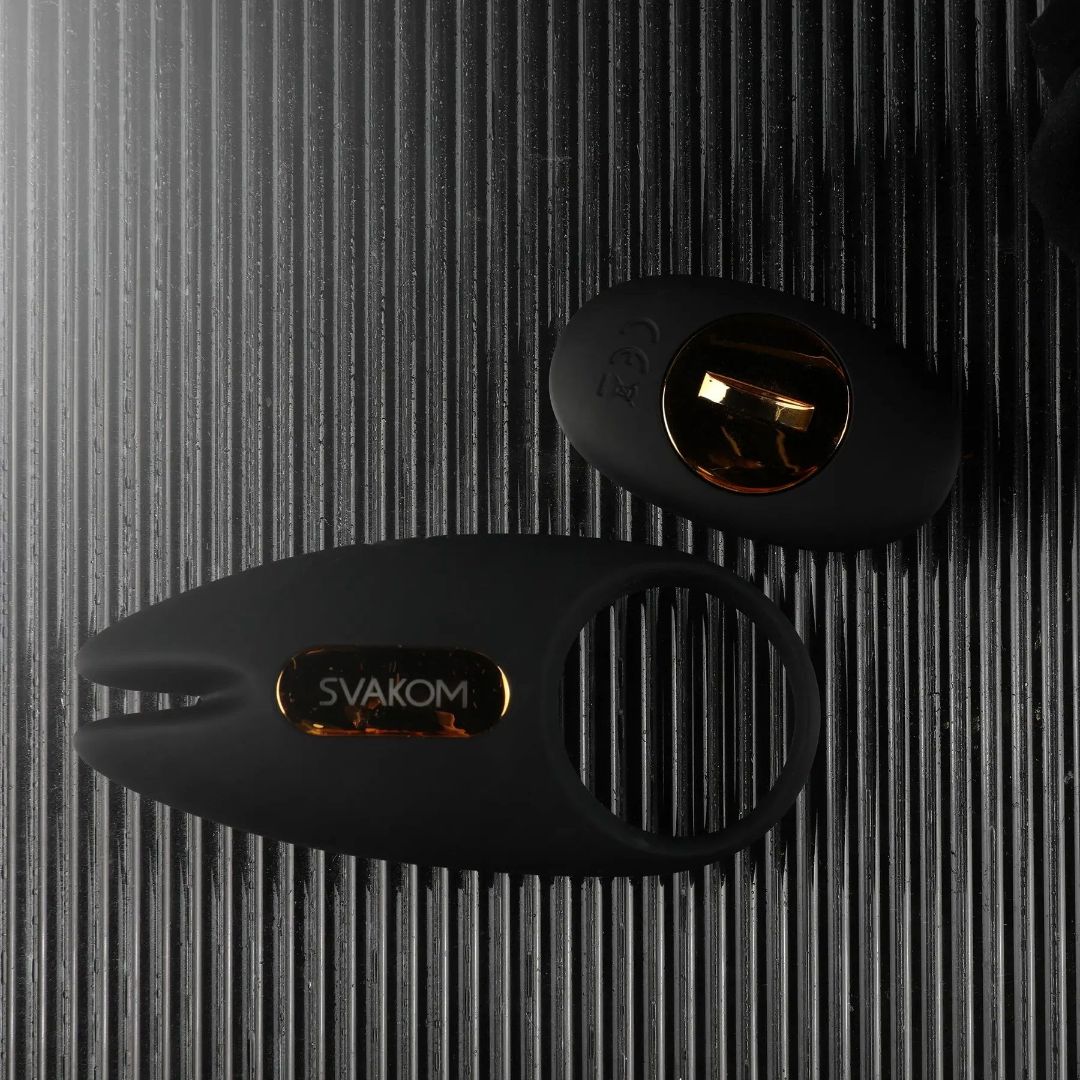 On a textured, dark surface lie two black silicone rings featuring gold accents. The larger ring, known as the "Svakom Winni 2 Penis Ring w/ App Control" from Svakom, showcases a sleek design and offers app-controlled vibrations, highlighting its role as an innovative couples' toy for personal wellness.