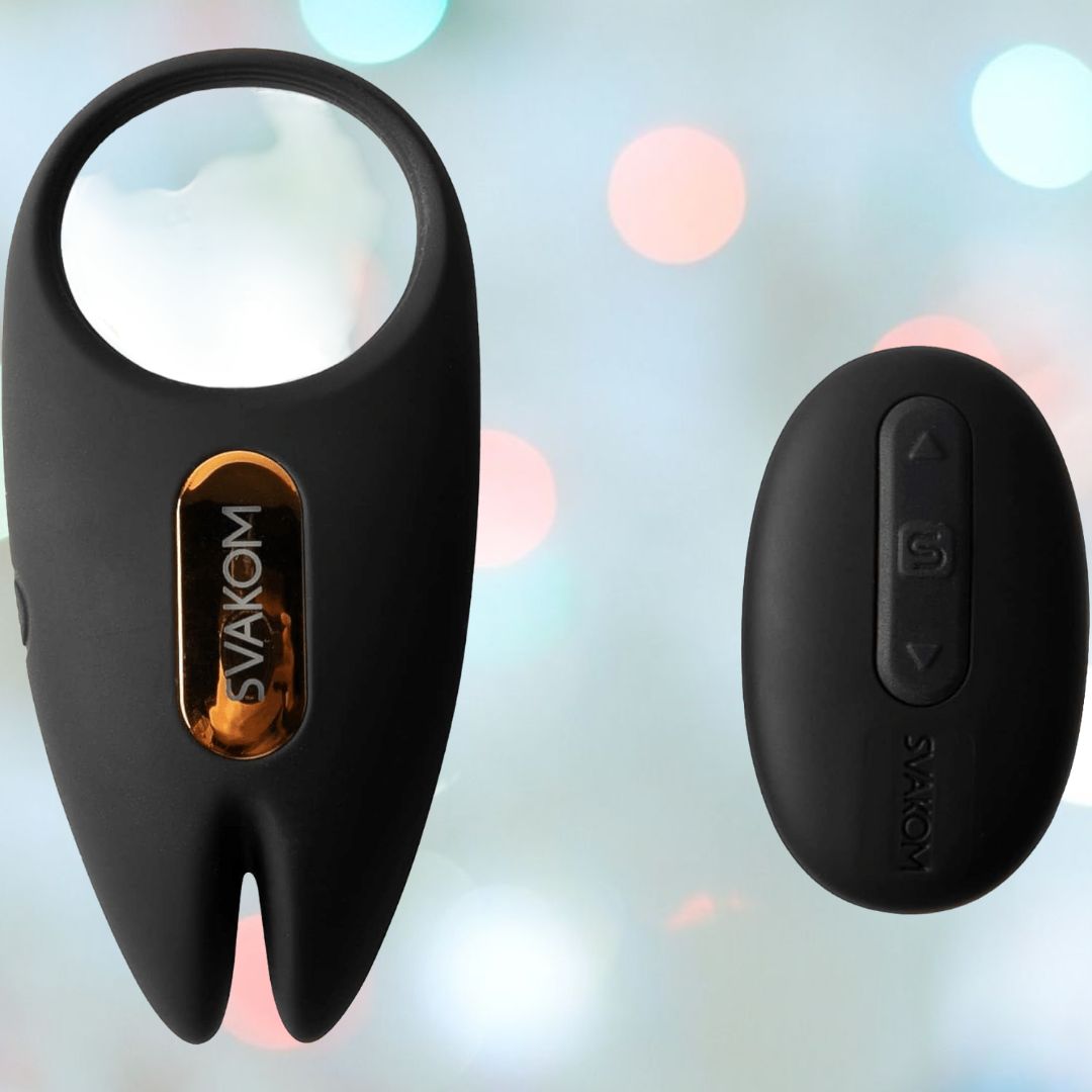 A Svakom Winni 2 Penis Ring with a black teardrop shape and gold accent is positioned near a smaller black remote control. Ideal for couples, this scene is set against a softly blurred background with pastel-colored lights.