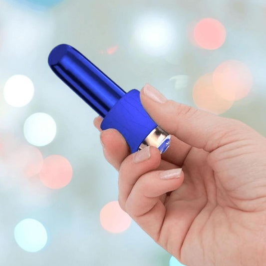 A hand holds the BMS Swan Maximum Rechargeable Bullet in blue, its metallic finish gleaming against a softly blurred background of colorful bokeh lights. 1080