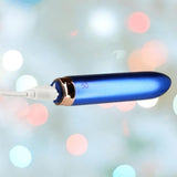 A close-up of the BMS Swan Maximum Rechargeable Bullet in blue, featuring a metallic ring near the end, being charged with a white USB cable against a pastel bokeh background.