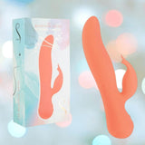 The Swan The Blossom Rabbit Vibrator - Coral by BMS, featuring a unique curved orange silicone design, is displayed beside its pastel box. The softly blurred background highlights the product.