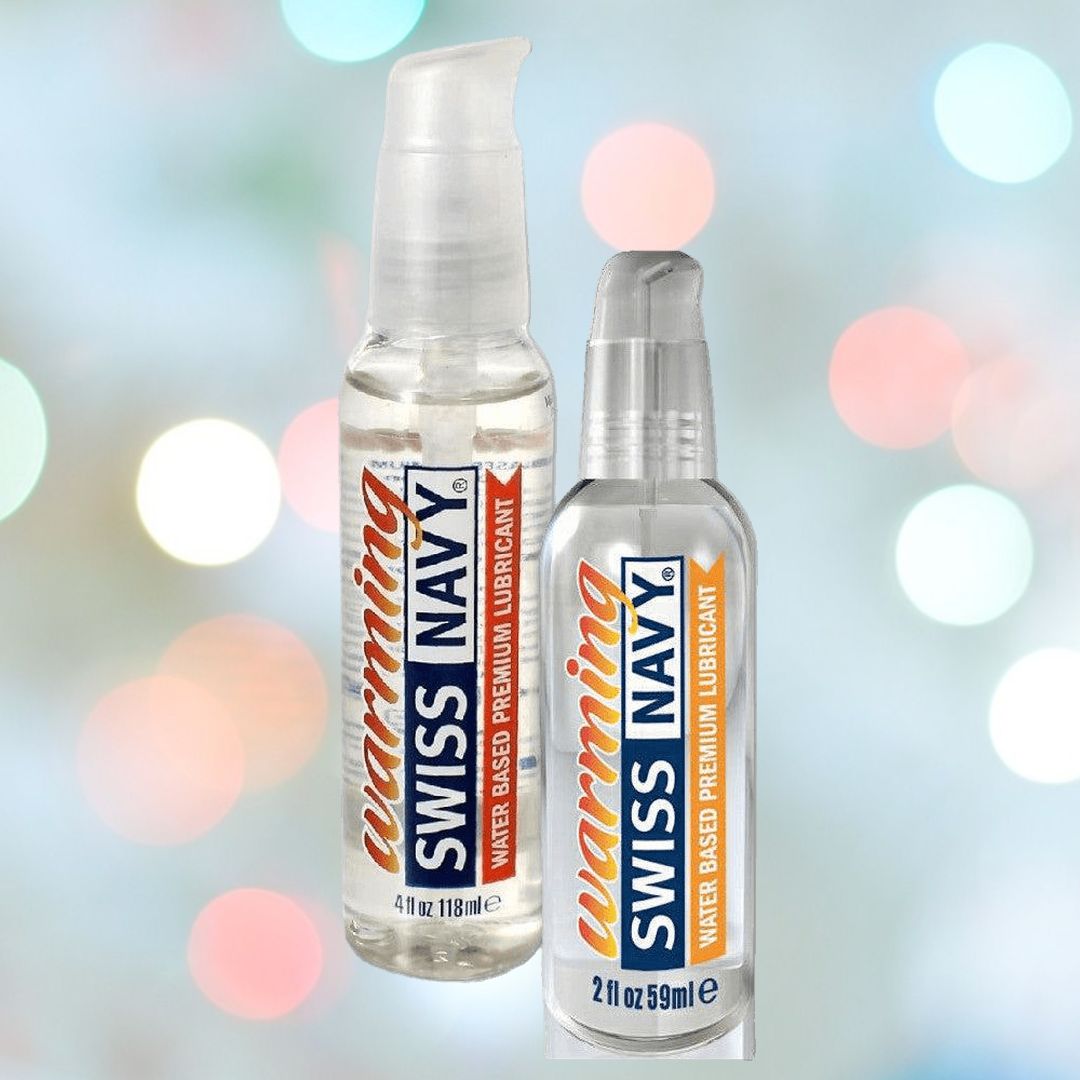 Two bottles of Swiss Navy Premium Warming Lubricant are showcased against a blurred background featuring colorful lights. One bottle contains 4 fl oz (118 ml) and the other 2 fl oz (59 ml), both offering the premium, soothing sensation of a water-based warming lubricant from Swiss Navy.